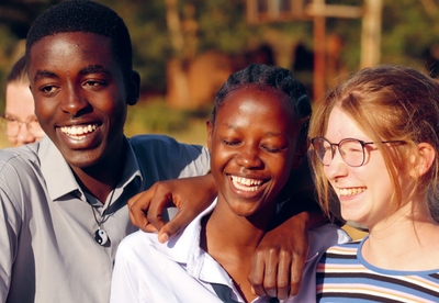 Foto: drei Jugendliche aus Afrika und Deutschland stehen zusammen, haben den Arm um die Schultern gelegt und lachen. 