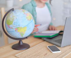 Foto: Im Vordergrund ein Globus. Im Hintergrund arbeitet eine Auszubildende am Notebook.